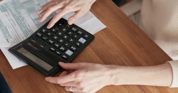 Mãos a usar uma calculadora numa mesa com documentos, faturas ou formulários.